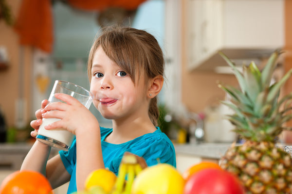 female kid drinking milk to fight cavity with mixed fresh fruits in front